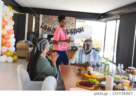 Family celebrating retirement at home with food and drinks, smiling and clapping 135536987