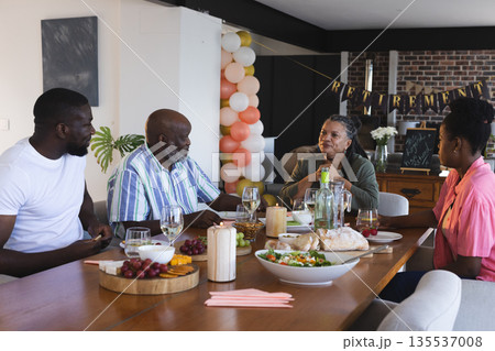 Family celebrating retirement with joyful conversation and delicious meal at home 135537008