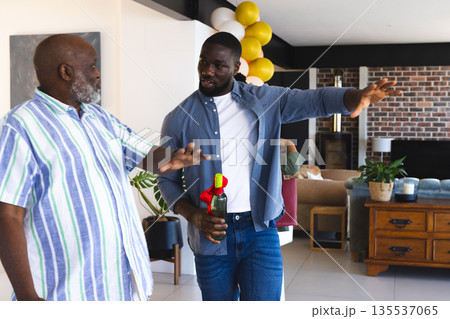 Two men in casual attire discussing while holding wine bottle at home Two men in casual attire discussing while holding wine bottle at home 135537065