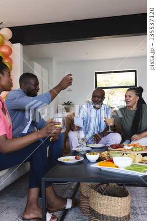 Friends toasting with drinks at home, enjoying festive gathering with snacks Friends toasting with drinks at home, enjoying festive gathering with snacks 135537120