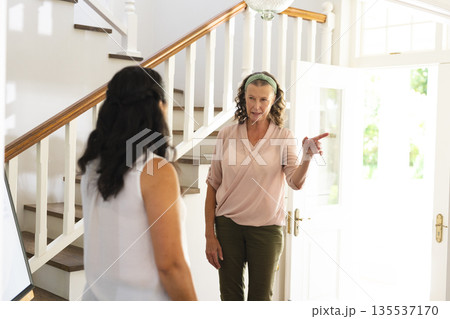 Senior woman wearing headphones giving directions to friend at home entrance Senior woman wearing headphones giving directions to friend at home entrance 135537170