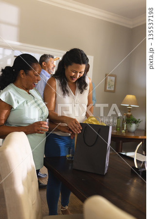 Smiling women opening gift bag at home during family celebration Smiling women opening gift bag at home during family celebration 135537198