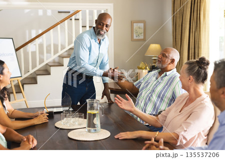 Senior friends celebrating at home, smiling and shaking hands around dining table Senior friends celebrating at home, smiling and shaking hands around dining table 135537206
