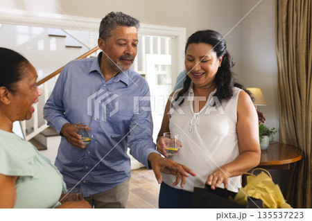 Smiling seniors celebrating at home, enjoying drinks and opening gifts together 135537223
