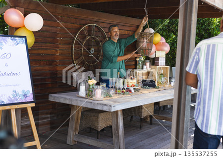 Man decorating outdoor party table with balloons and drinks for celebration Man decorating outdoor party table with balloons and drinks for celebration 135537255
