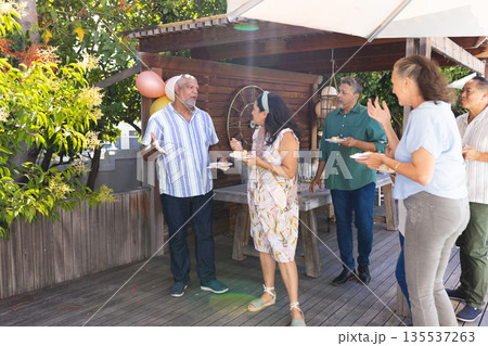 Seniors enjoying outdoor birthday party, sharing laughter and cake on wooden deck Seniors enjoying outdoor birthday party, sharing laughter and cake on wooden deck 135537263