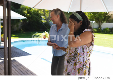 Women laughing and enjoying sunny day by pool in backyard gathering 135537270