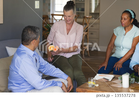 Senior woman giving flowers to man while sitting with friends at home 135537278