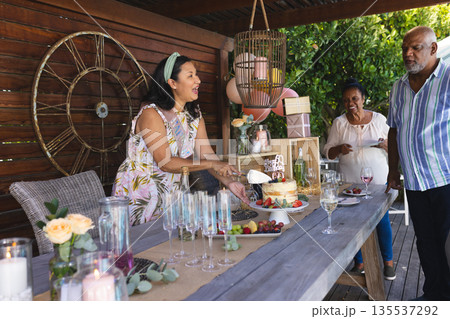 Family celebrating birthday outdoors, woman cutting cake while others enjoy wine Family celebrating birthday outdoors, woman cutting cake while others enjoy wine 135537292