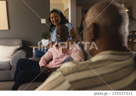 African American man sitting on sofa smiling with friends at home gathering African American man sitting on sofa smiling with friends at home gathering 135537311