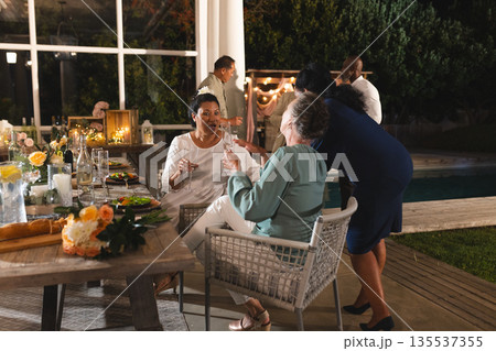 Seniors enjoying outdoor celebration, laughing and toasting with friends by pool 135537355