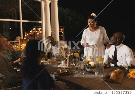 Giving speech at outdoor dinner party, African American woman engaging attentive guests Giving speech at outdoor dinner party, African American woman engaging attentive guests 135537359