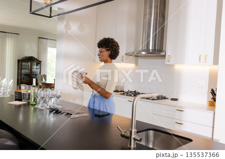 Woman in modern kitchen drying glassware, preparing for elegant dinner party 135537366