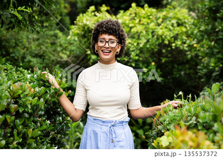 Smiling woman enjoying nature in lush garden, surrounded by vibrant greenery Smiling woman enjoying nature in lush garden, surrounded by vibrant greenery 135537372