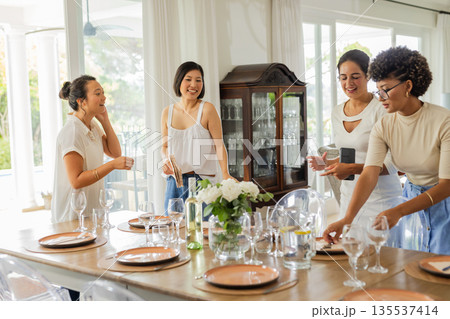 Setting elegant dining table with glassware and flowers, women preparing celebration 135537414