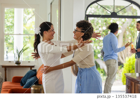 Bride in white dress hugging friend warmly at home during wedding celebration 135537418