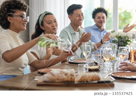 Pouring wine, friends laughing around dinner table with bread and flowers 135537425
