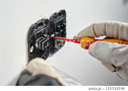 Hand using screwdriver to fix electrical wall switch 135538596