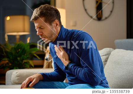 Sick man sitting on sofa holding chest with pain at home Sick man sitting on sofa holding chest with pain at home 135538739