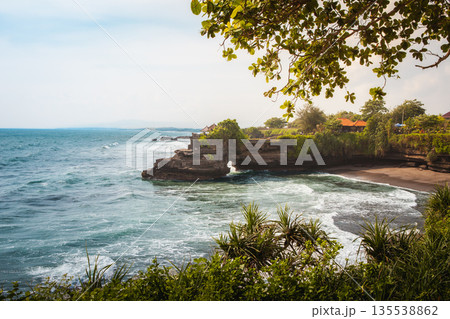 Scenic coastal landscape near Tanah Lot, dramatic ocean waves crashing on rugged cliffs. Tropical foliage and lush green vegetation, perfect for Bali travel, nature escape stock photography Scenic coastal landscape near Tanah Lot, dramatic ocean waves crashing on rugged cliffs. Tropical foliage and lush green vegetation, perfect for Bali travel, nature escape stock photography 135538862
