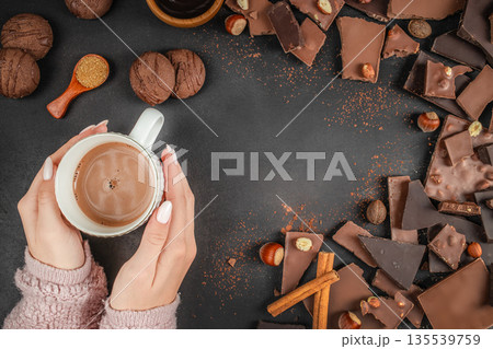 Hands holding hot chocolate cup surrounded by chocolate pieces top view 135539759