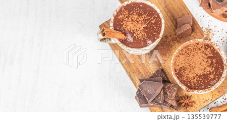 Hot chocolate cups with cocoa powder and cinnamon on wooden board, top view with copy space 135539777