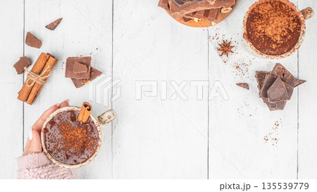 Top view of hot chocolate with cocoa powder and cinnamon held in hand on white wooden background with copy space Top view of hot chocolate with cocoa powder and cinnamon held in hand on white wooden background with copy space 135539779