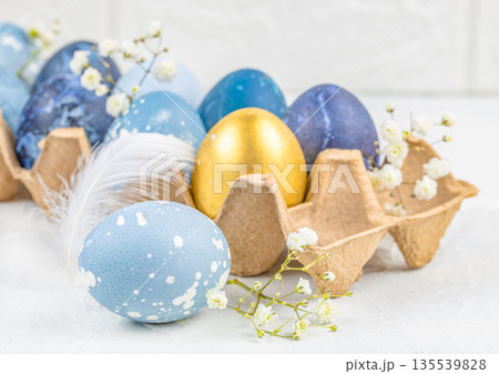 Elegant Easter eggs in cardboard carton with blue and gold colors, spring flowers and soft light Elegant Easter eggs in cardboard carton with blue and gold colors, spring flowers and soft light 135539828
