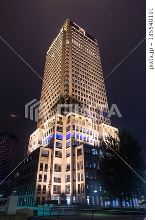 Business skyscraper at night. Modern evening building. Skyscraper in city. City downtown with skyscraper. Office building in business district. Skyscraper building architecture. Perspective view Business skyscraper at night. Modern evening building. Skyscraper in city. City downtown with skyscraper. Office building in business district. Skyscraper building architecture. Perspective view 135540191