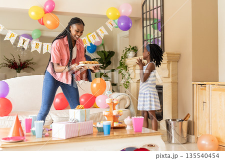 Celebrating birthday, African American mother and child with cupcakes and decorations 135540454