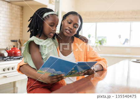 Reading storybook, African American mother bonding with daughter at kitchen counter 135540475