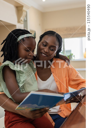 Mother and daughter reading book together, African American family bonding at home 135540490