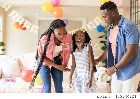 Family celebrating birthday at home, decorating with balloons and colorful banners Family celebrating birthday at home, decorating with balloons and colorful banners 135540521