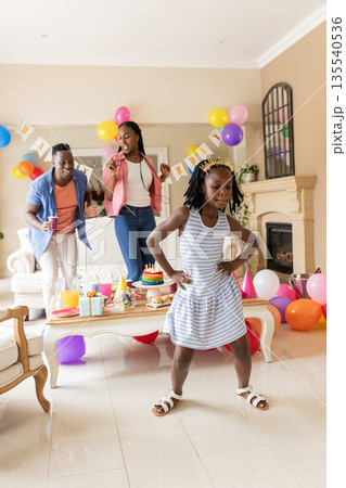 Family celebrating birthday at home, young girl dancing with parents cheering 135540536