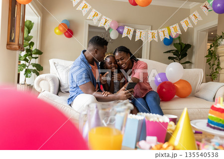 African American family celebrating birthday at home, smiling and hugging on sofa African American family celebrating birthday at home, smiling and hugging on sofa 135540538