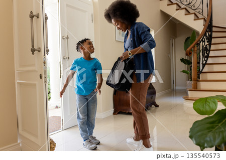 African American mother and son entering home, smiling and carrying backpack 135540573