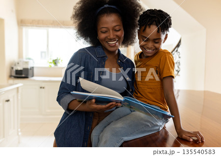 Mother and child reading book together in cozy kitchen, sharing joyful moment Mother and child reading book together in cozy kitchen, sharing joyful moment 135540583