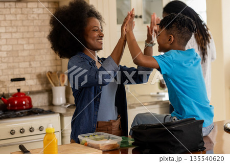 African American mother and son high-fiving in kitchen, enjoying morning together African American mother and son high-fiving in kitchen, enjoying morning together 135540620