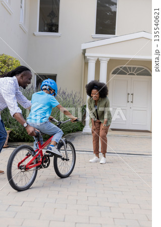 African American parents teaching child to ride bicycle in front of house 135540621