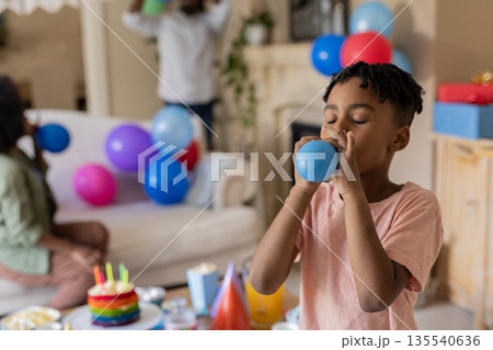 African American boy blowing up balloon at birthday party with family at home 135540636