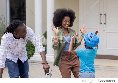 Child wearing helmet high-fiving mom, African American family playing outdoors 135540644