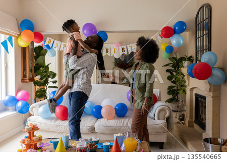 Father lifting son in air at birthday party, mother smiling in living room Father lifting son in air at birthday party, mother smiling in living room 135540665