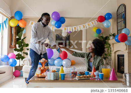 Decorating room with colorful balloons and snacks, African American couple celebrating birthday Decorating room with colorful balloons and snacks, African American couple celebrating birthday 135540668