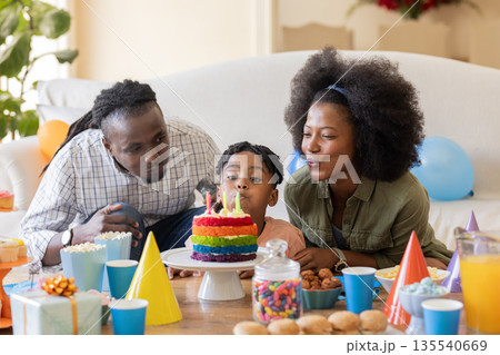 Family celebrating birthday at home, blowing out candles on colorful cake together Family celebrating birthday at home, blowing out candles on colorful cake together 135540669
