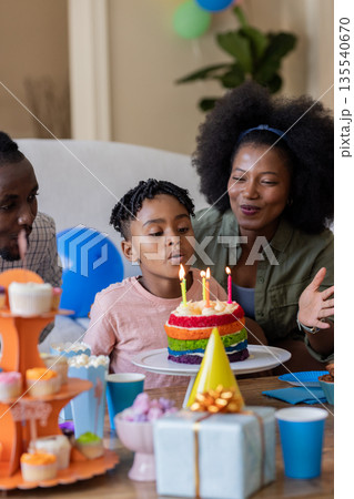African American family celebrating birthday with child blowing out candles on cake African American family celebrating birthday with child blowing out candles on cake 135540670