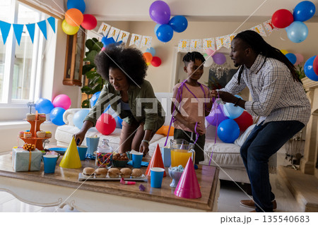 African American family celebrating birthday at home with balloons and party hats African American family celebrating birthday at home with balloons and party hats 135540683