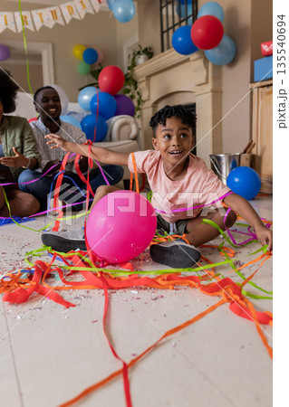 Child playing with colorful streamers and balloons at home, celebrating joyfully 135540694