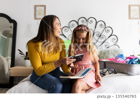 Mother and daughter packing suitcase together, smiling and sharing joyful moment Mother and daughter packing suitcase together, smiling and sharing joyful moment 135540765
