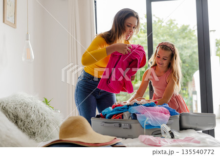 Mother and daughter packing suitcase together at home, preparing for vacation Mother and daughter packing suitcase together at home, preparing for vacation 135540772