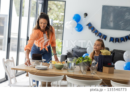 Celebrating birthday, woman placing cake on table while girl eagerly watching Celebrating birthday, woman placing cake on table while girl eagerly watching 135540773